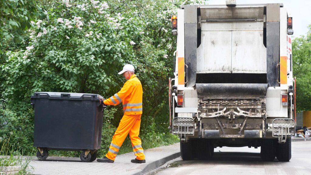 A bin man collecting rubbish from a black bin that will go to landfill. 