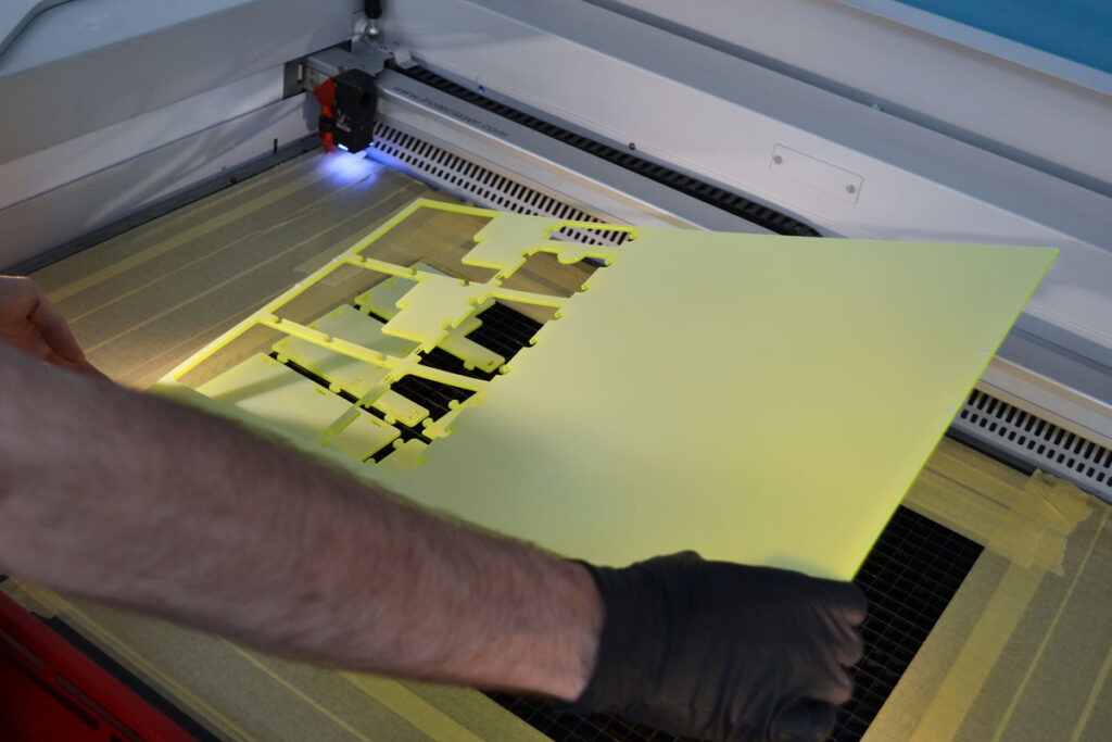 Image of precision laser cutting services. The hand of a laser cutting machine operator removing the cut components from a sheet of plastic.